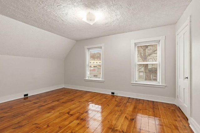 additional living space featuring hardwood / wood-style floors, vaulted ceiling, and a textured ceiling