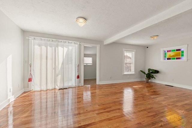 spare room featuring beamed ceiling and light wood-type flooring