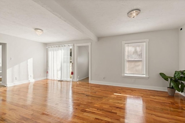 empty room with beamed ceiling, wood-type flooring, a healthy amount of sunlight, and a textured ceiling