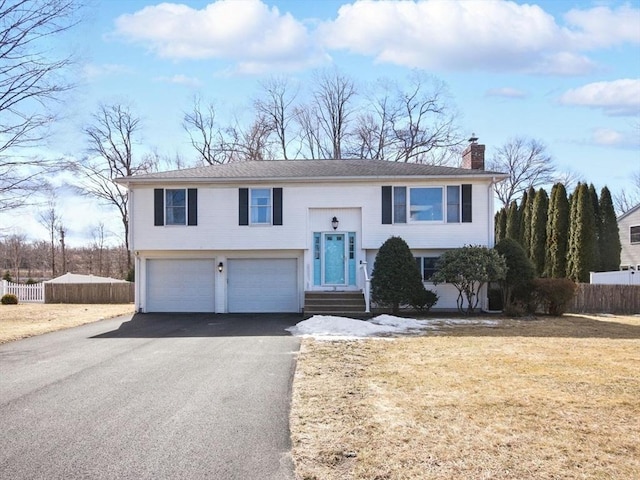 bi-level home featuring fence, aphalt driveway, a front yard, a chimney, and a garage