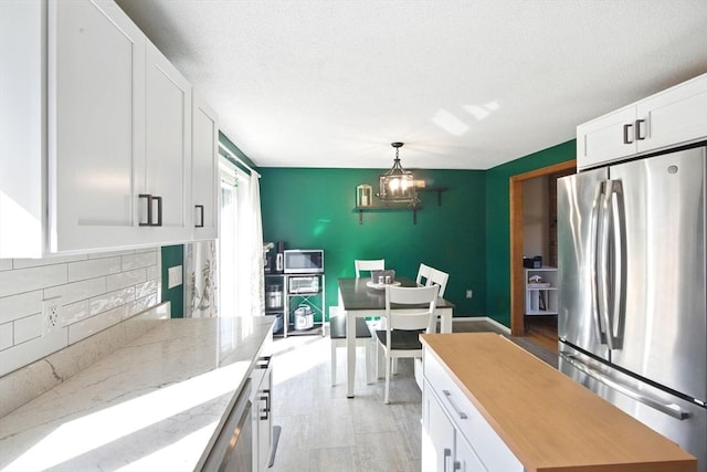 kitchen featuring tasteful backsplash, light stone countertops, appliances with stainless steel finishes, a notable chandelier, and white cabinetry