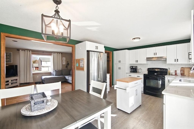 kitchen with electric range, a notable chandelier, under cabinet range hood, freestanding refrigerator, and decorative backsplash