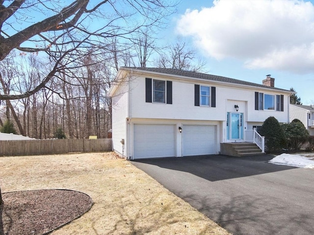 split foyer home featuring aphalt driveway, an attached garage, a chimney, and fence