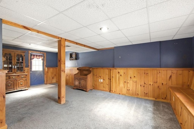 basement with a drop ceiling, carpet, wood walls, and wainscoting