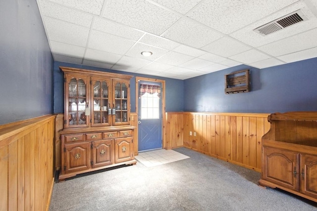 interior space with a wainscoted wall, light colored carpet, visible vents, and a paneled ceiling