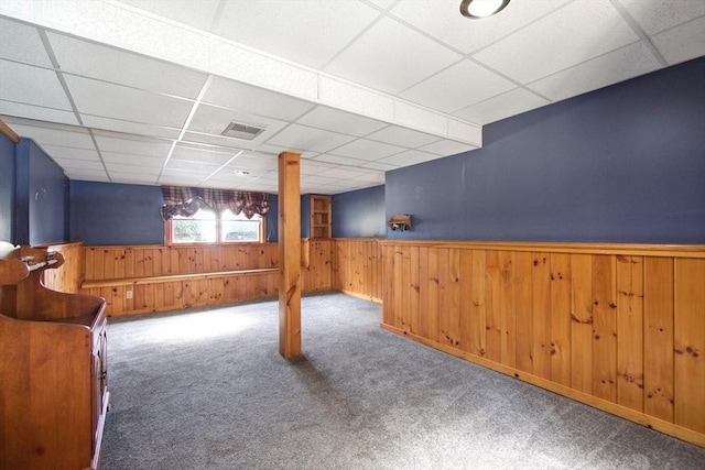 basement featuring visible vents, carpet, a wainscoted wall, wood walls, and a paneled ceiling