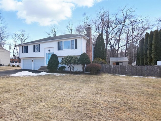 bi-level home featuring fence, a front yard, a chimney, driveway, and an attached garage