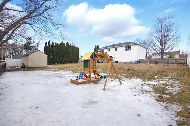 snowy yard with an outdoor structure, a playground, fence, and a shed