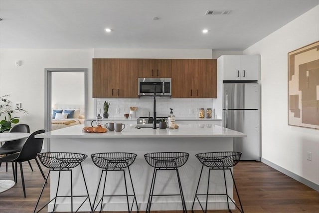 kitchen featuring a breakfast bar, light countertops, decorative backsplash, appliances with stainless steel finishes, and dark wood-style floors