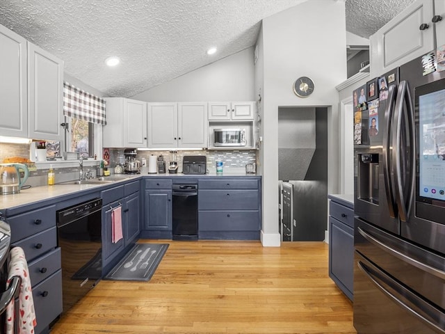 kitchen featuring vaulted ceiling, light wood-type flooring, backsplash, white cabinetry, and appliances with stainless steel finishes