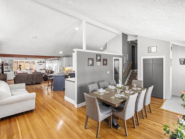 dining space featuring a textured ceiling, light hardwood / wood-style flooring, and vaulted ceiling with beams