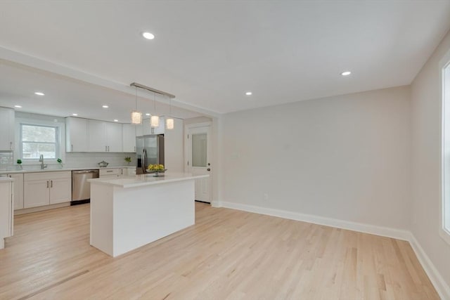 kitchen with a kitchen island, white cabinets, light countertops, appliances with stainless steel finishes, and pendant lighting