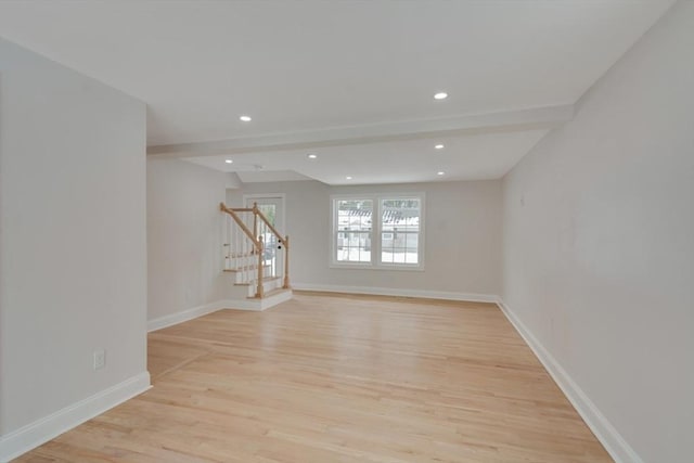 spare room featuring light wood-type flooring, beam ceiling, stairway, and baseboards