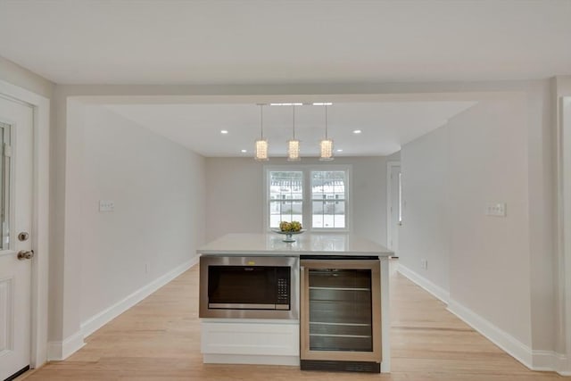 kitchen with pendant lighting, beverage cooler, stainless steel microwave, and light wood-style flooring