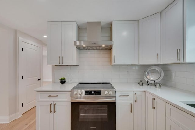 kitchen with light countertops, stainless steel range with electric cooktop, wall chimney range hood, and white cabinetry