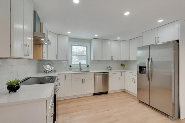 kitchen featuring stainless steel appliances, light countertops, white cabinets, a sink, and wall chimney range hood