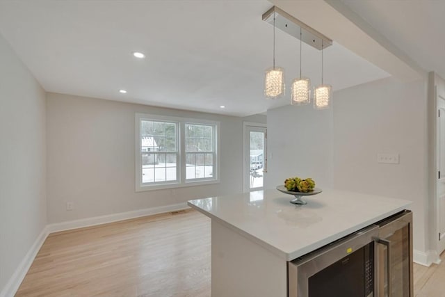 kitchen featuring beverage cooler, light wood-style flooring, a kitchen island, light countertops, and pendant lighting