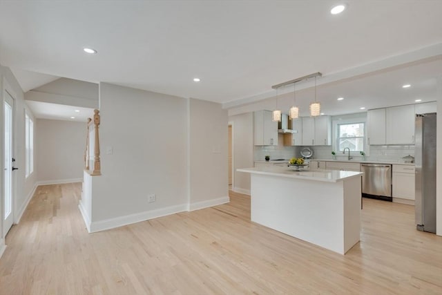 kitchen with a kitchen island, appliances with stainless steel finishes, hanging light fixtures, light countertops, and white cabinetry