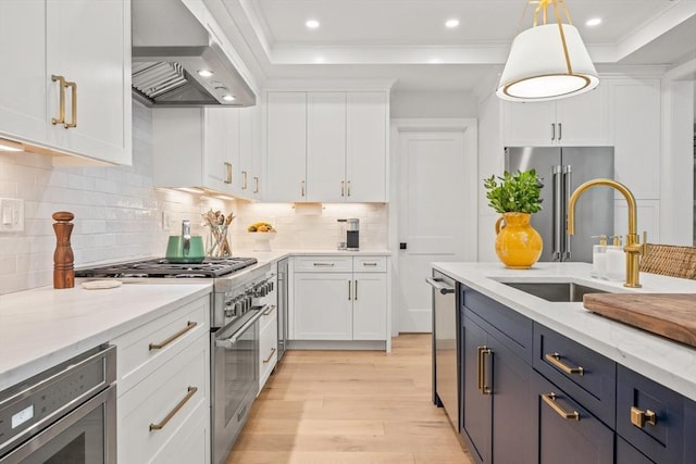 kitchen featuring ornamental molding, premium appliances, white cabinetry, wall chimney exhaust hood, and a sink