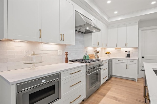 kitchen with wall chimney range hood, light stone countertops, light wood-type flooring, stainless steel appliances, and white cabinetry