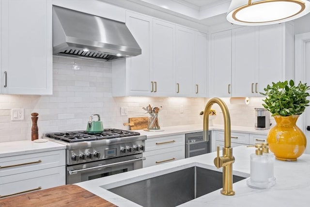 kitchen with backsplash, stainless steel range, white cabinetry, and wall chimney range hood