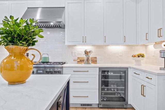 kitchen with light stone countertops, wine cooler, white cabinetry, wall chimney exhaust hood, and tasteful backsplash