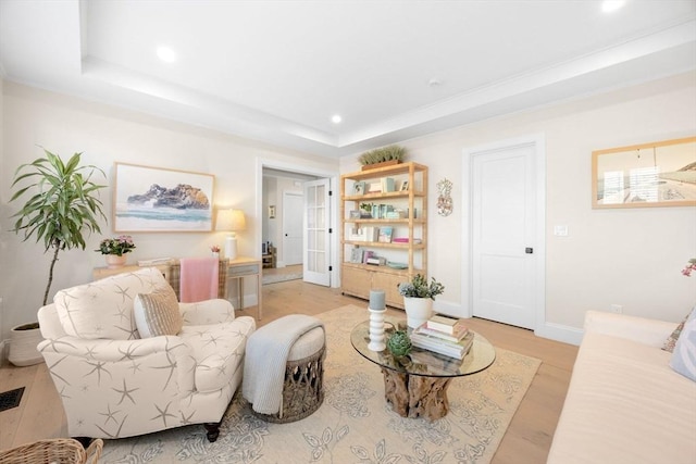 living room with recessed lighting, a tray ceiling, baseboards, and light wood finished floors