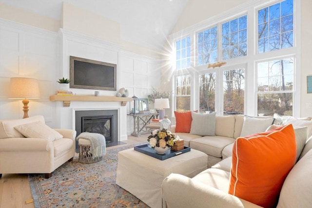 living room featuring a fireplace with flush hearth, high vaulted ceiling, wood finished floors, and a decorative wall