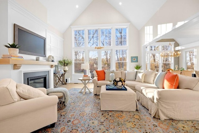 living room featuring a notable chandelier, a glass covered fireplace, high vaulted ceiling, and wood finished floors