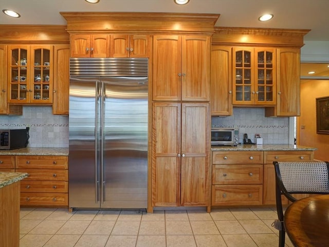 kitchen with backsplash, light stone counters, light tile patterned floors, and appliances with stainless steel finishes