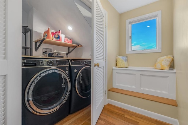 clothes washing area with laundry area, washing machine and dryer, baseboards, and light wood-style floors