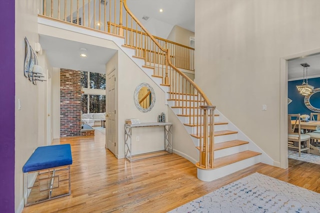 staircase with baseboards, an inviting chandelier, wood finished floors, and a towering ceiling