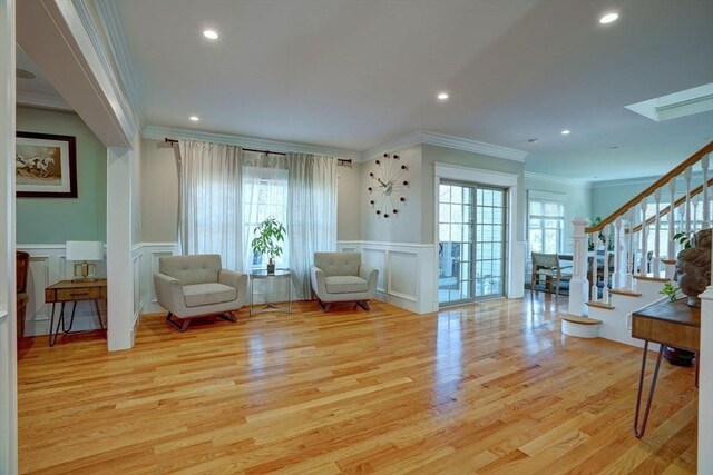 living area with a decorative wall, ornamental molding, plenty of natural light, wood finished floors, and stairway