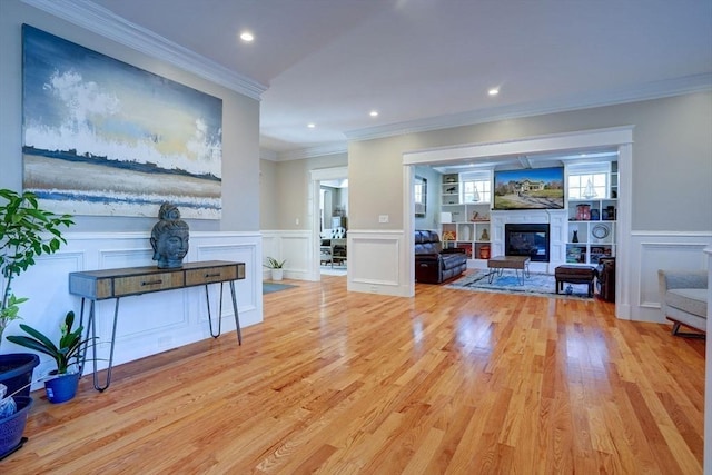 living room featuring a decorative wall, crown molding, a glass covered fireplace, light wood-style floors, and a wainscoted wall