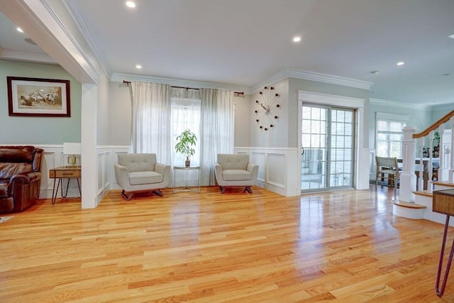 living area with a decorative wall, ornamental molding, plenty of natural light, wood finished floors, and a wainscoted wall