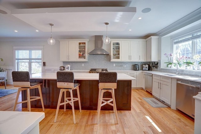 kitchen with wall chimney exhaust hood, stainless steel dishwasher, a sink, crown molding, and healthy amount of natural light
