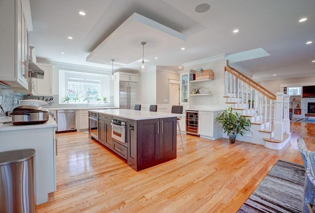 kitchen with stainless steel appliances, beverage cooler, light countertops, healthy amount of natural light, and ornamental molding