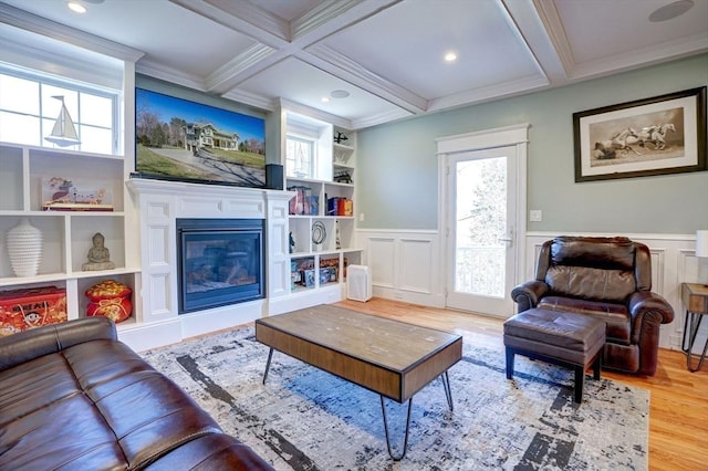 living room with wood finished floors, beamed ceiling, coffered ceiling, a glass covered fireplace, and ornamental molding