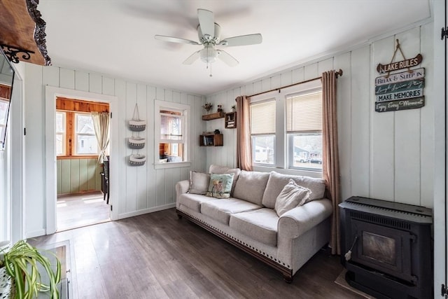 living room with wood finished floors, a wood stove, baseboards, and ceiling fan