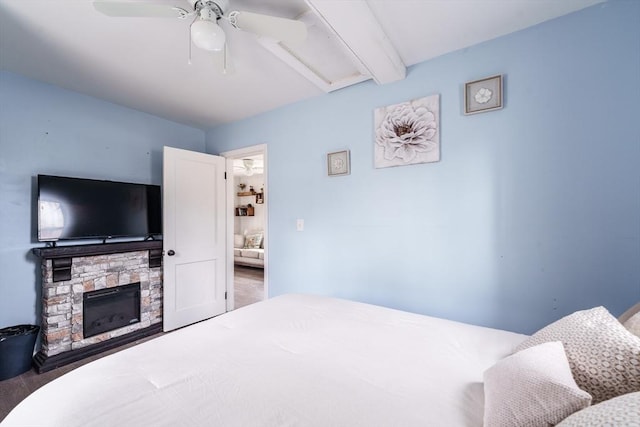 bedroom featuring a ceiling fan, a stone fireplace, and beam ceiling