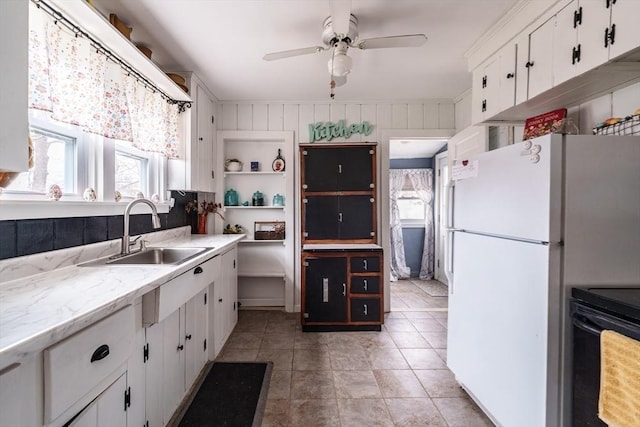 kitchen with a sink, black electric range, ceiling fan, white cabinets, and freestanding refrigerator