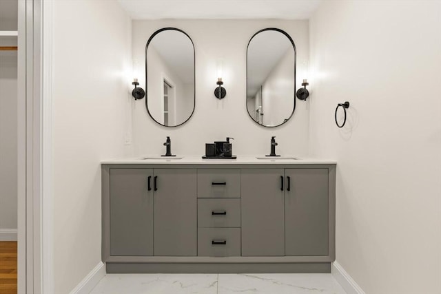 full bath with marble finish floor, double vanity, a sink, and baseboards