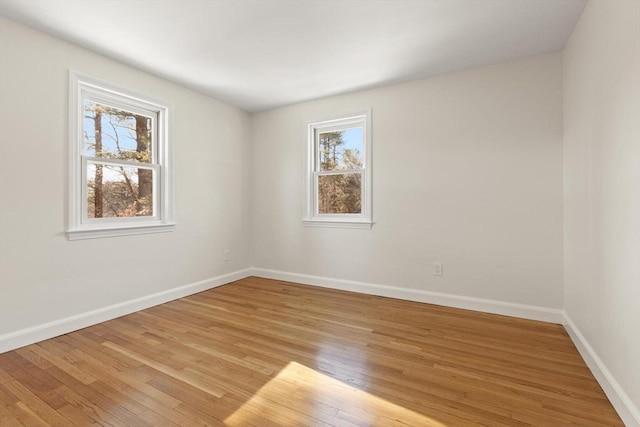 spare room with baseboards, a wealth of natural light, and light wood-style floors