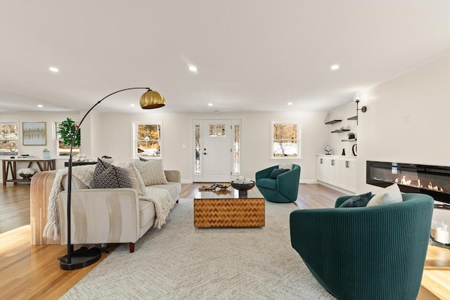 living area with recessed lighting, plenty of natural light, a glass covered fireplace, and light wood-style floors