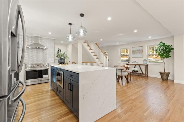 kitchen with stainless steel appliances, light wood-style flooring, wall chimney range hood, and tasteful backsplash