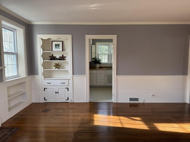 empty room with ornamental molding, built in shelves, dark wood-type flooring, and sink