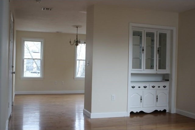 spare room with visible vents, baseboards, a notable chandelier, and wood finished floors