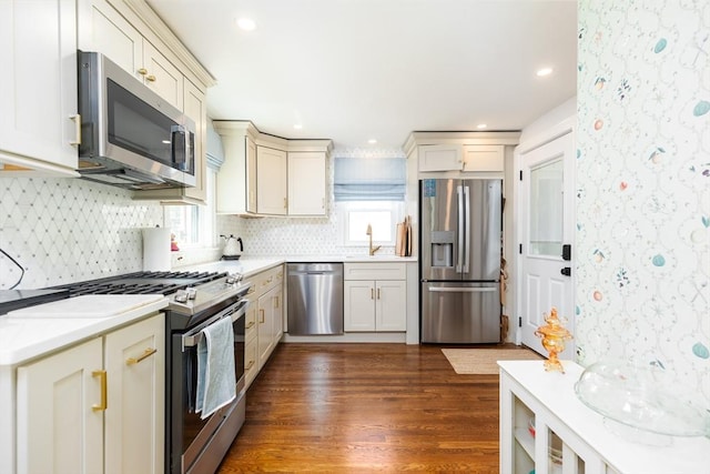 kitchen featuring appliances with stainless steel finishes, a sink, light countertops, decorative backsplash, and dark wood-style floors