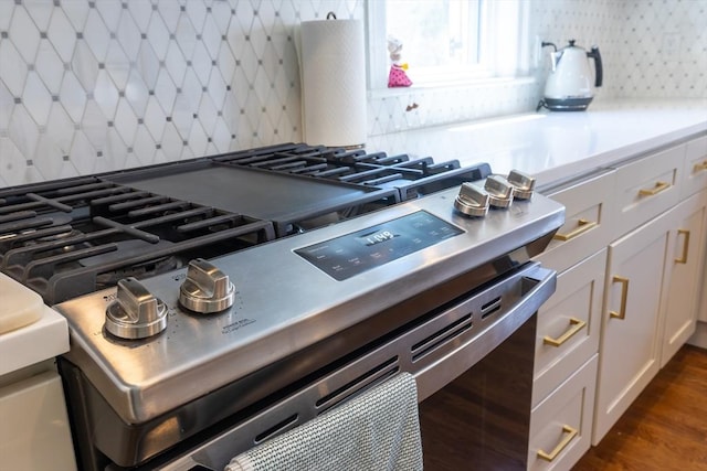 room details featuring white cabinets, dark wood-style flooring, light countertops, decorative backsplash, and gas range