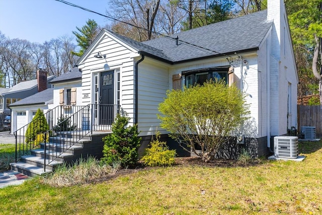 bungalow-style home with roof with shingles, cooling unit, a front yard, and a garage